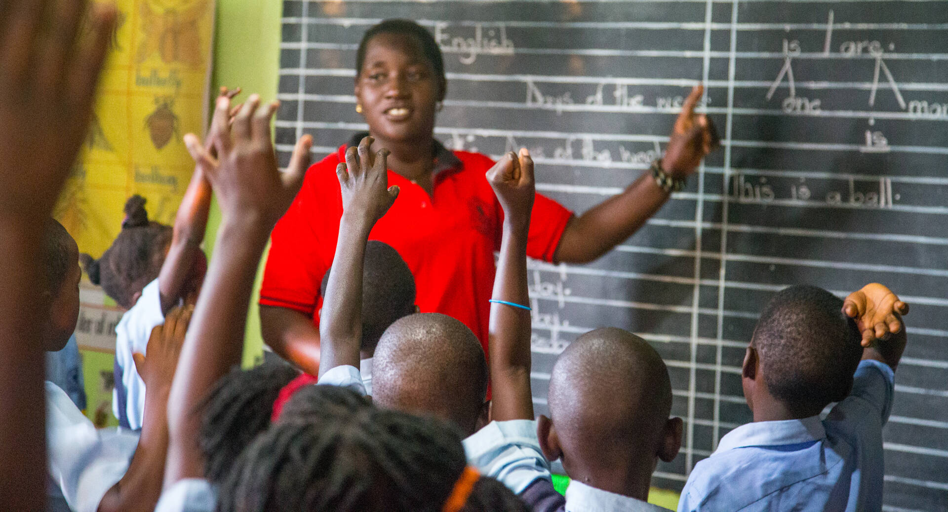 Learners raising their hands to answer a question in an Affordable Non-state school. Photo Credit: Opportunity International